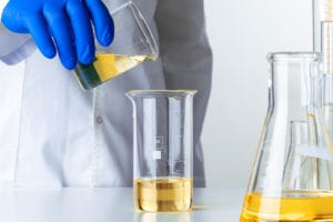 Scientist or doctor in blue gloves pouring some yellow liquid into a flask